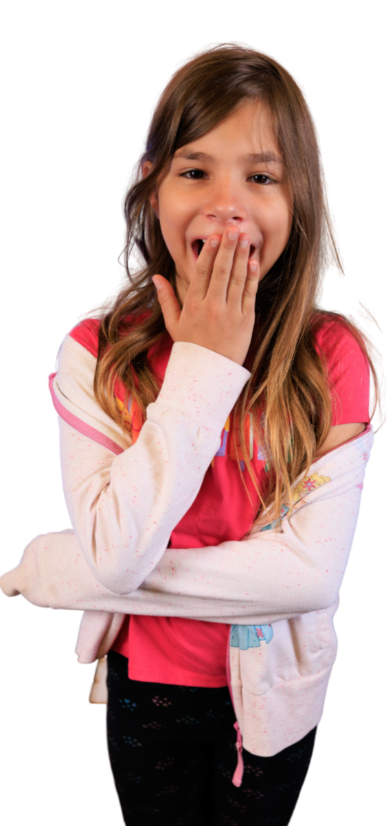 A young girl with long brown hair covering her ears, wearing a pink t-shirt and a light pink hoodie with colorful details, covering her mouth with her hand and smiling.