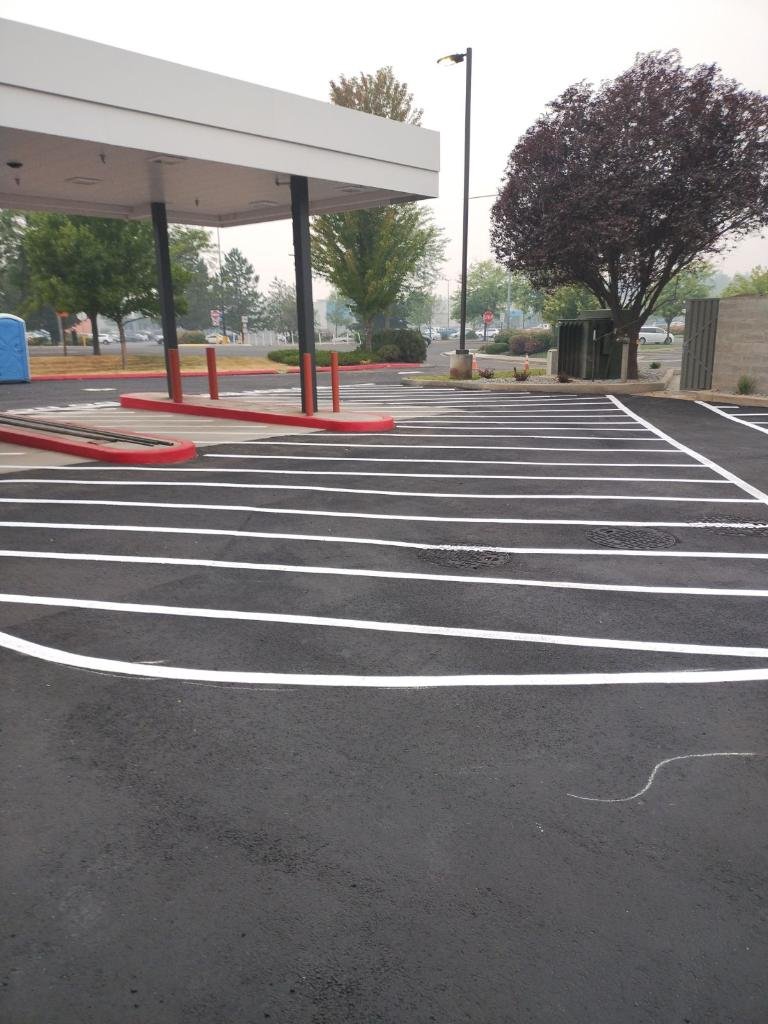 Empty parking lot with freshly painted white lines, red protective barriers, a small canopy, trees, a blue trash can, and a trash bin. Overcast sky.