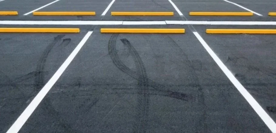 Empty parking lot with tire marks on the asphalt and yellow parking blocks.