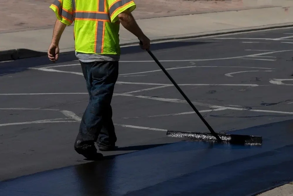 Worker in safety vest applying black asphalt to a parking lot.