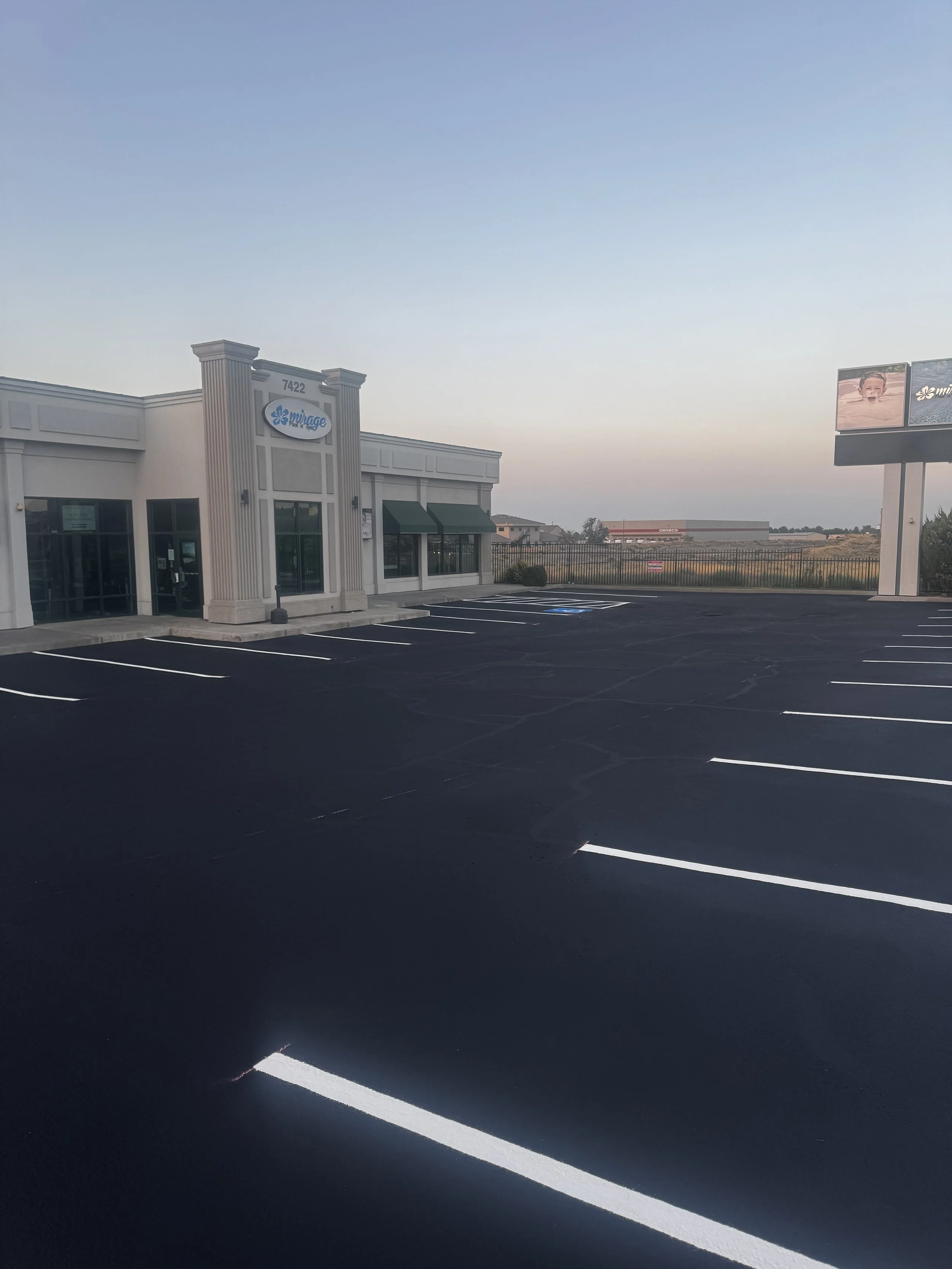 Empty parking lot in front of a commercial building with a sign that reads Mirage, under a clear sky.