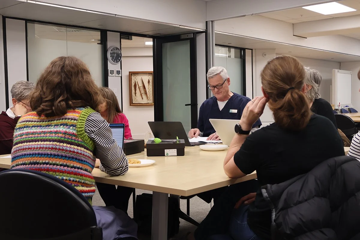 People sitting around a conference table in a meeting room, listening to a man in scrubs.