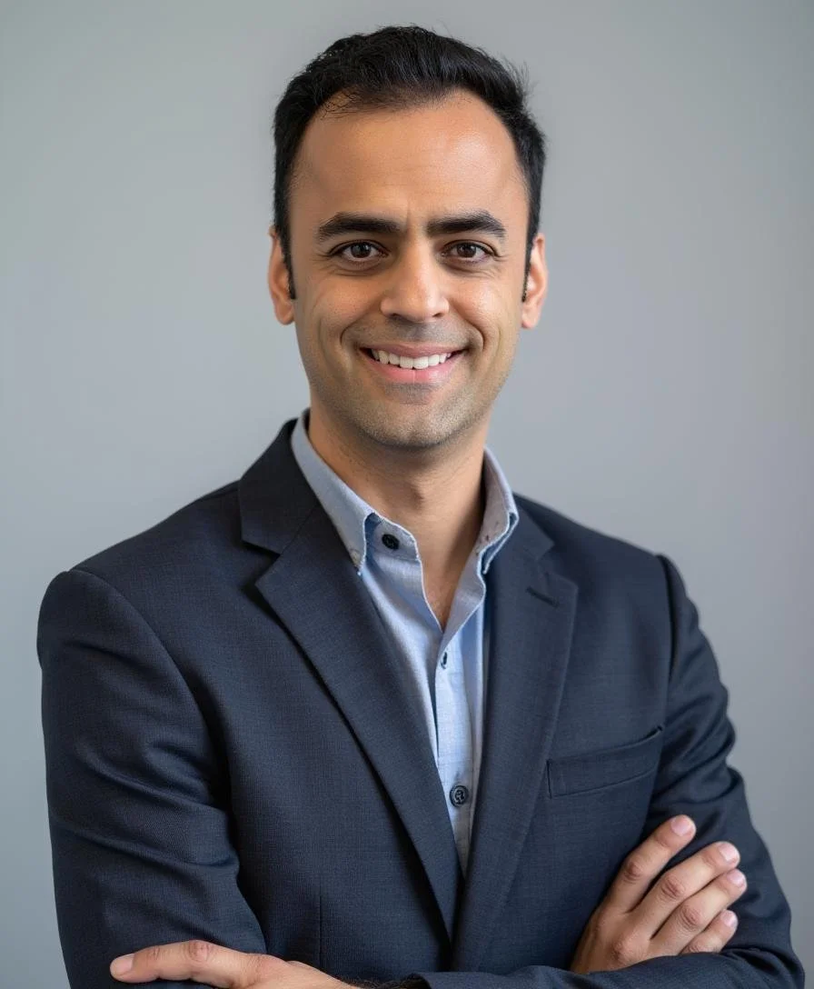 A professional man in a suit smiling with his arms crossed against a plain background.