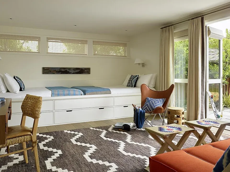 Bright living room with built-in daybed, patterned rug, leather and fabric chairs, and sliding glass doors to outdoor area.