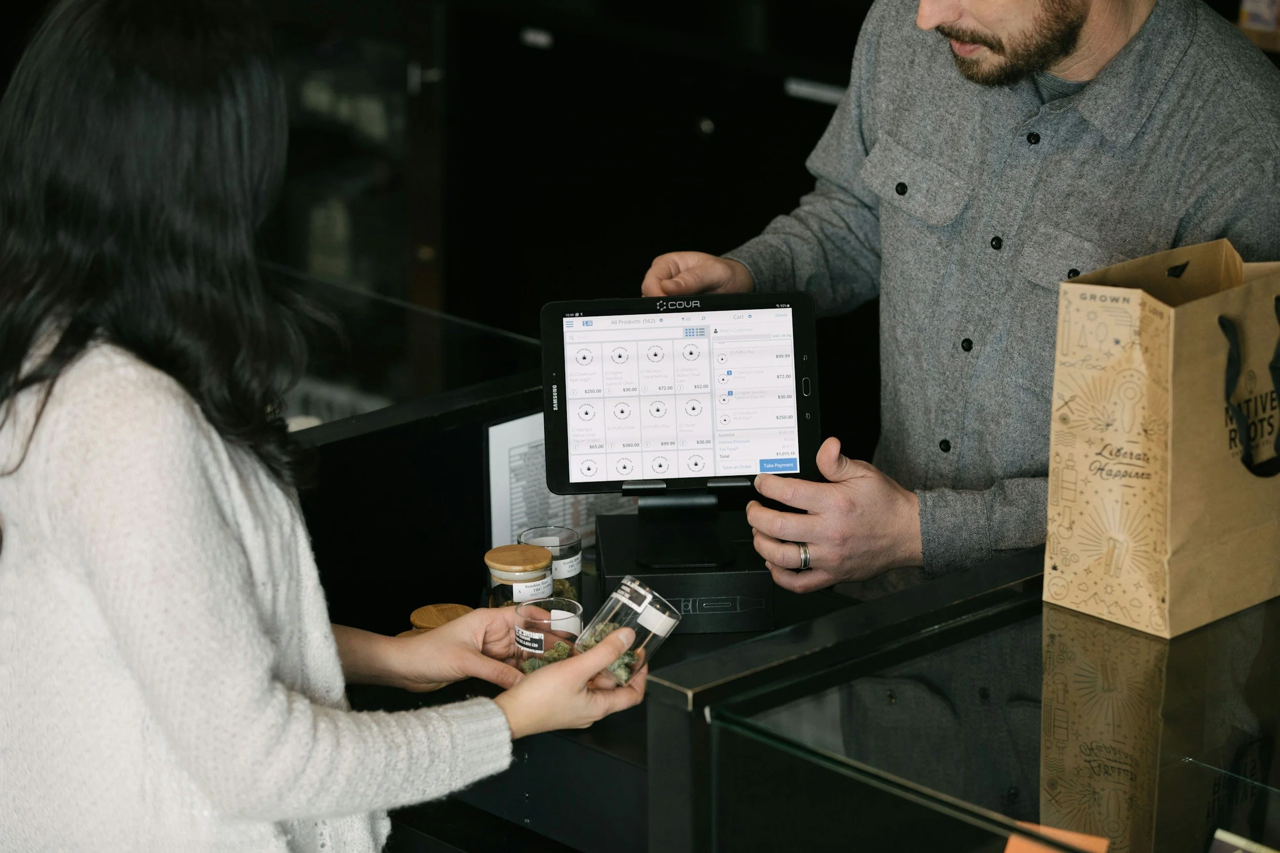 A customer at a register with a tablet POS system, purchasing edible product samples from a clerk.