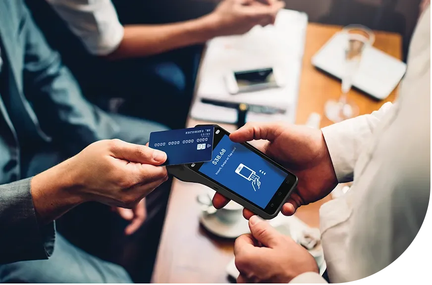 Person in a gray suit using a smartphone to scan a blue credit card in a restaurant or cafe.