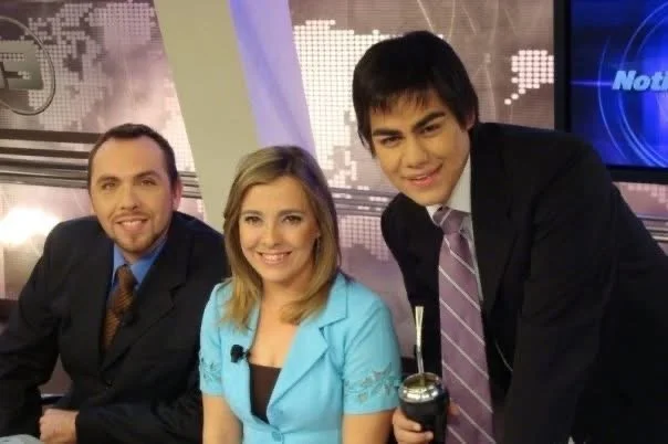 Tres personas en un estudio de noticias, dos hombres y una mujer, todos vestidos formalmente.