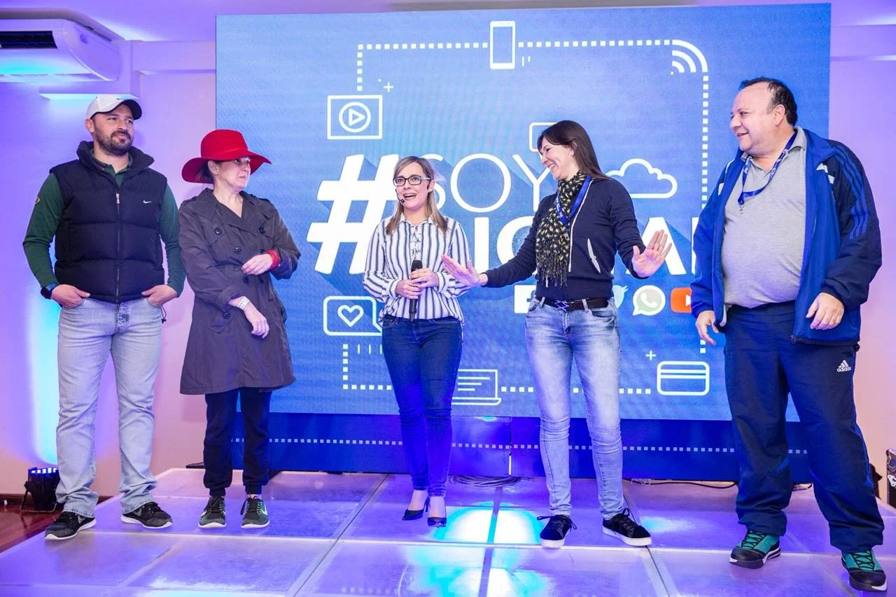 Cinco personas de pie en un escenario con una pantalla grande detrás que dice '#HOY' y 'HISTORIA'. Tres de ellas son mujeres y dos hombres, uno de ellos con micrófono, y todos parecen estar participando en un evento o presentación.