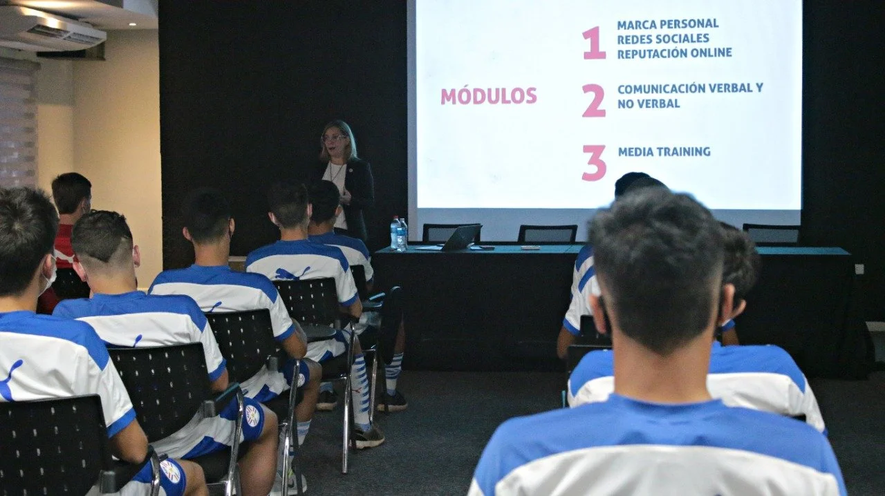 Grupo de jóvenes en una clase o capacitación, con una mujer que presenta una diapositiva en una pantalla