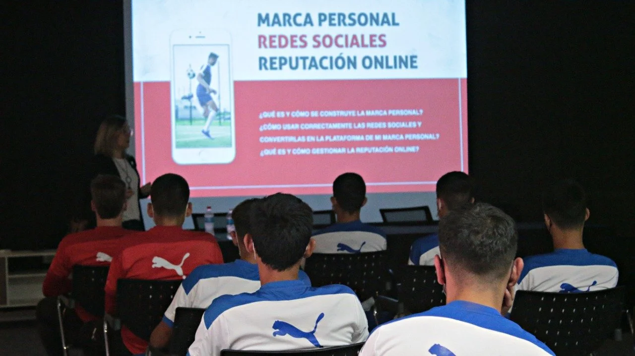 Una presentación con diapositivas sobre marca personal, redes sociales y reputación en línea, con un grupo de personas vistiendo camisetas de Puma en una sala oscura.