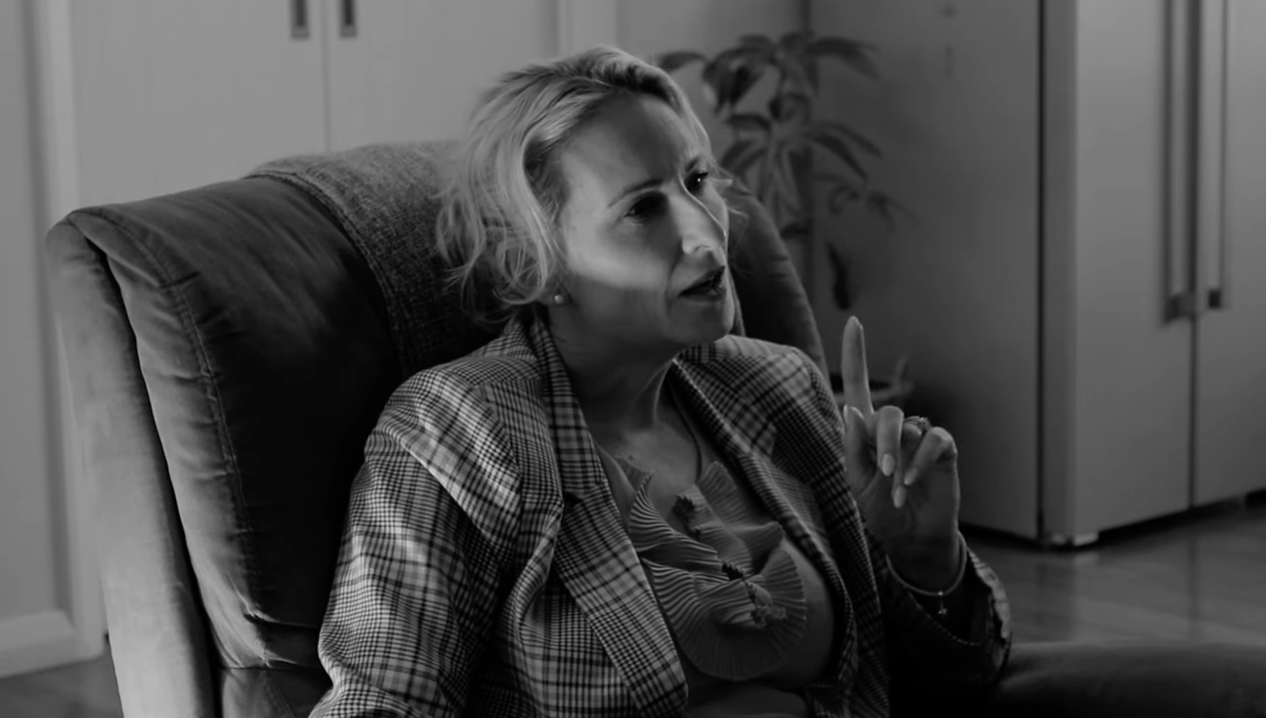 A black and white photo of a woman sitting on an armchair, talking and making a point with her index finger raised.