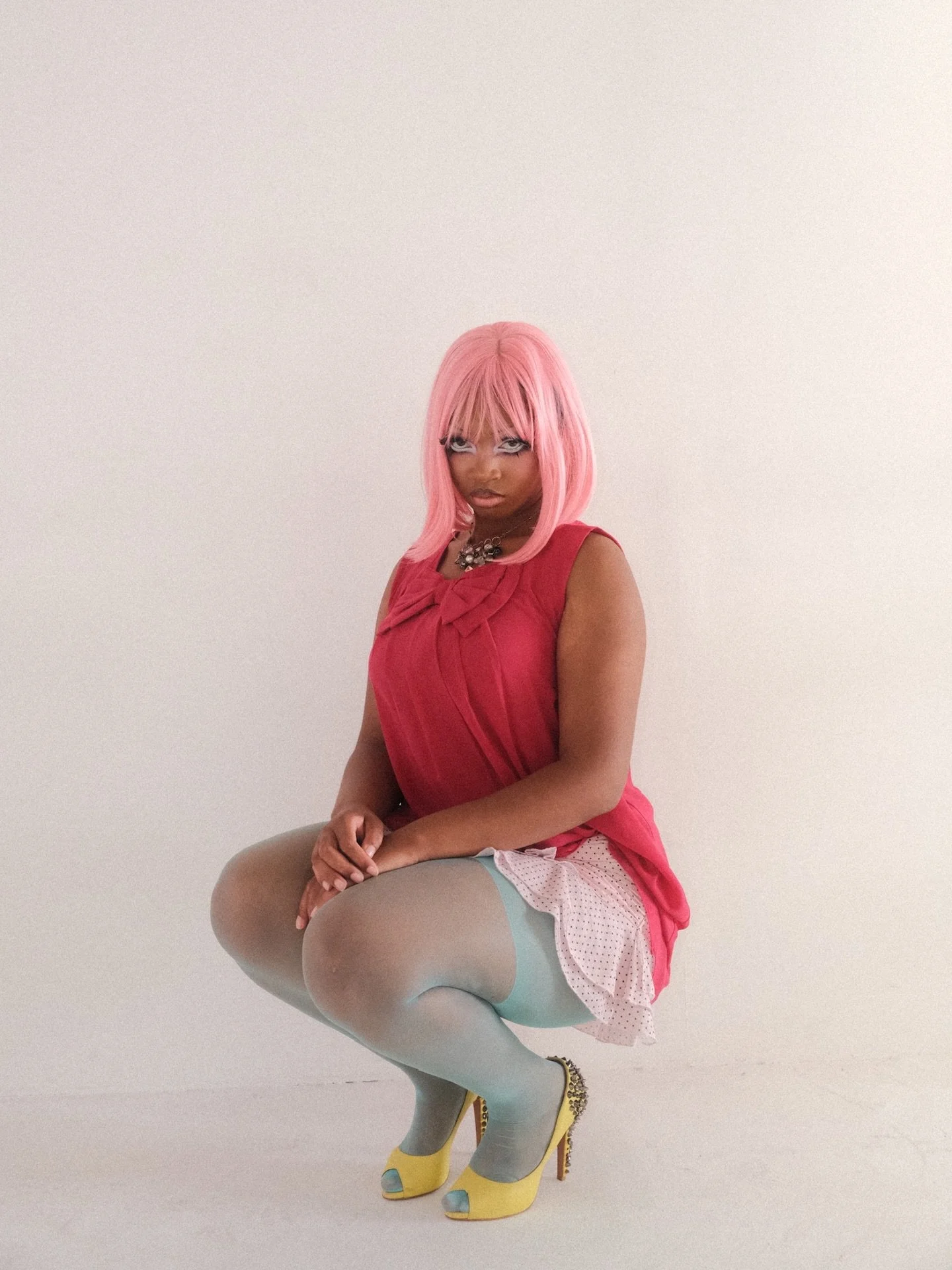A Lemon Time model with pink hair, wearing a red dress, white tights, and yellow high heels with rhinestones, poses against a plain white wall.