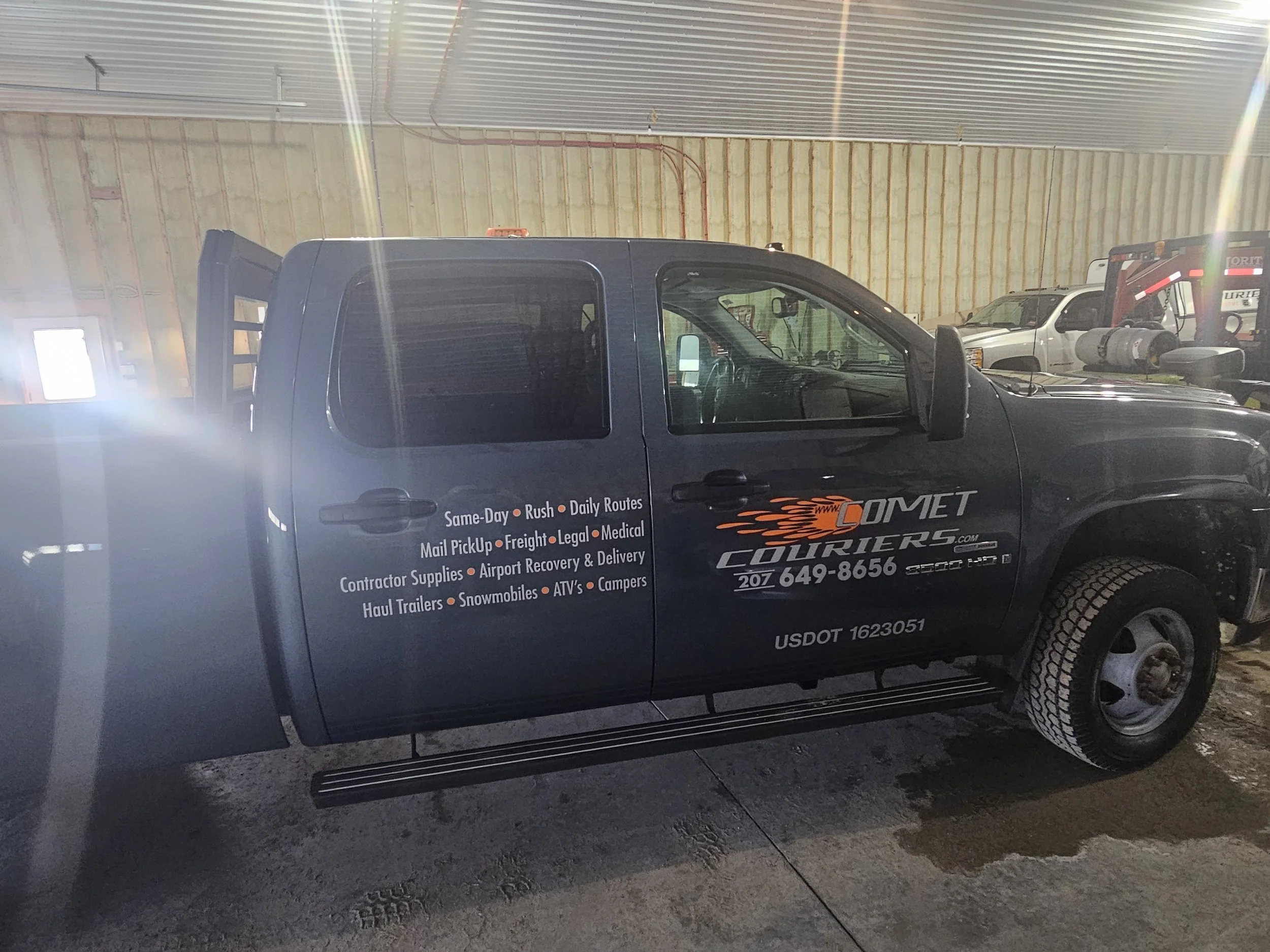 Black pickup truck inside a warehouse with the logo and contact information for Comet Couriers, listing various delivery services on the door.