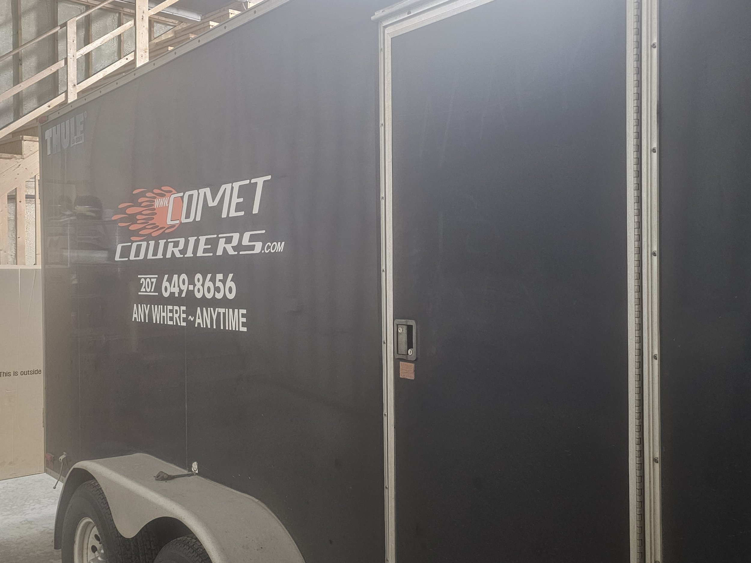 A black enclosed cargo trailer with the logo and contact information of Comet Couriers, including phone number and slogan 'ANY WHERE~ANYTIME.'