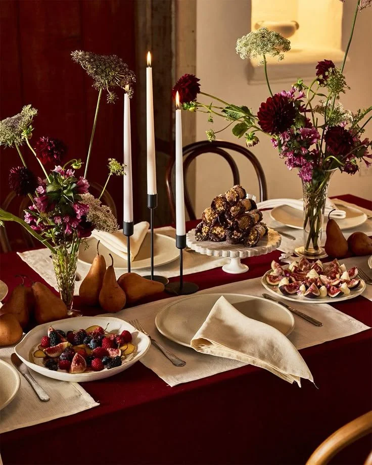 A festive table set with plates of fruit desserts, flowers, and tall candles.