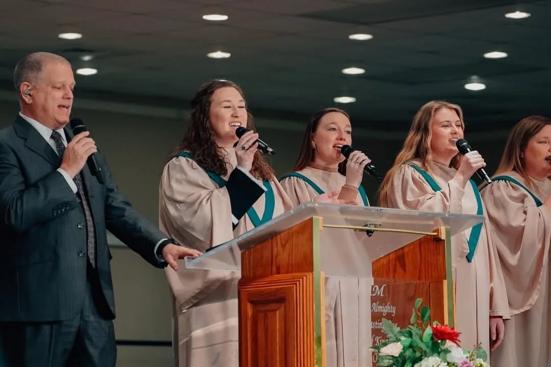 A Worship Minister and Praise Team females singing on stage with microphones, standing behind a wooden podium.
