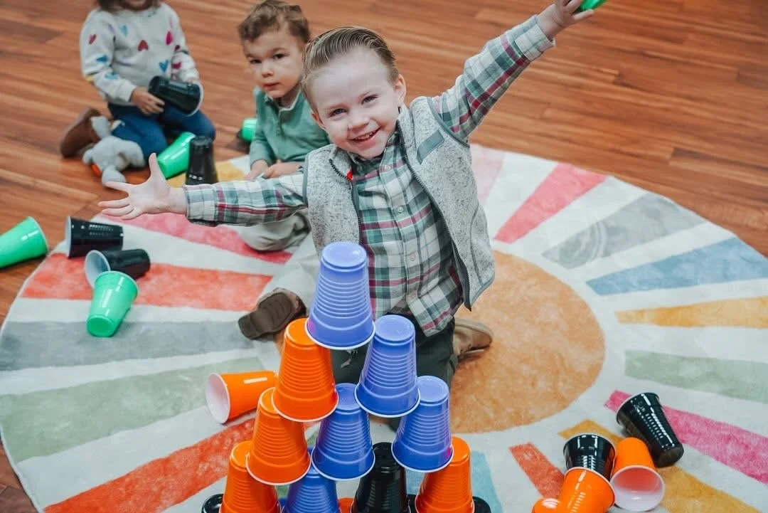 Three children at Morningside's Gateway Kids Ministry playing with plastic cups stacked into a pyramid on a colorful rug.