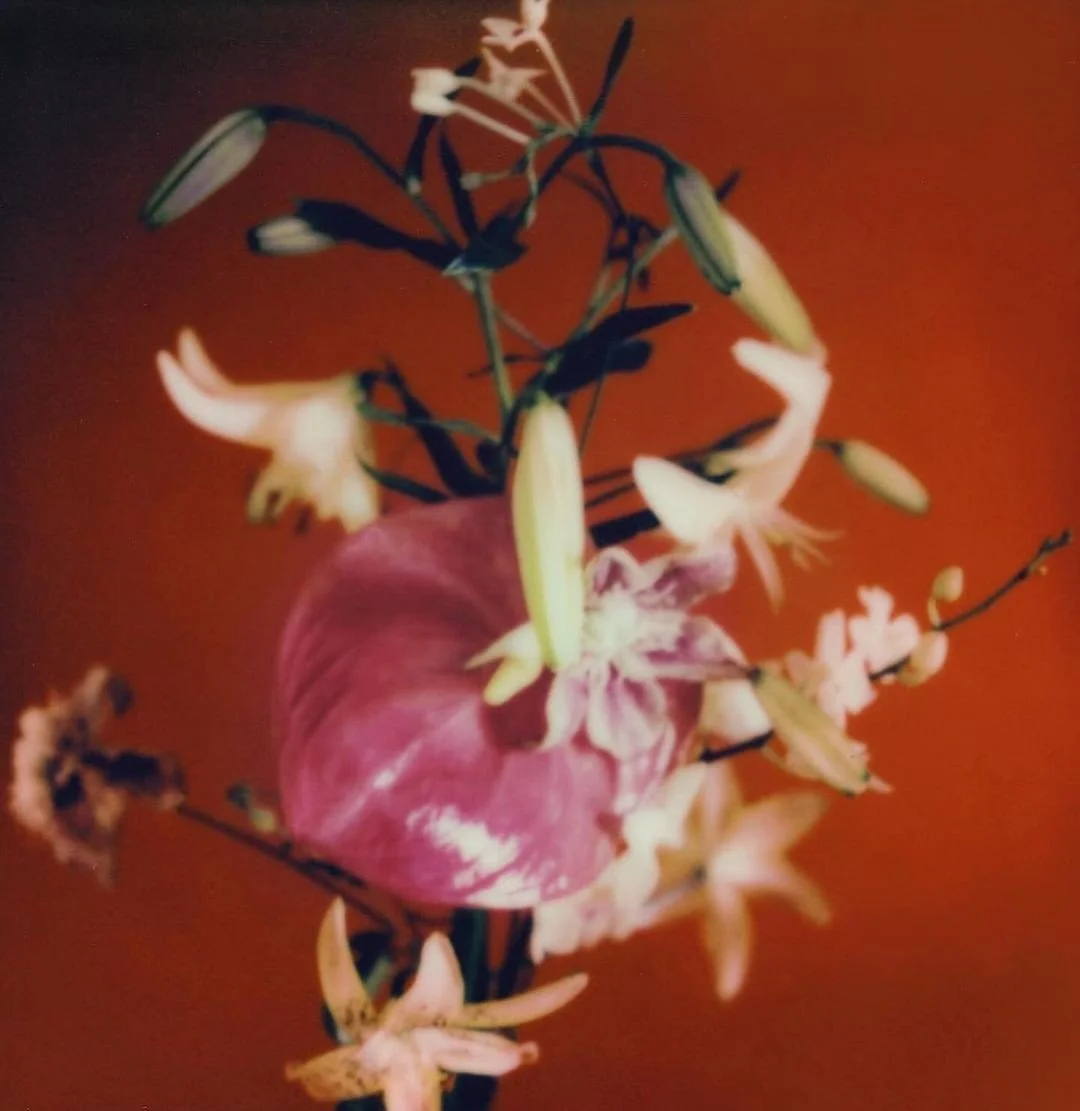 Blurred image of a bouquet with a pink heart-shaped flower and cream-colored lilies against an orange background.