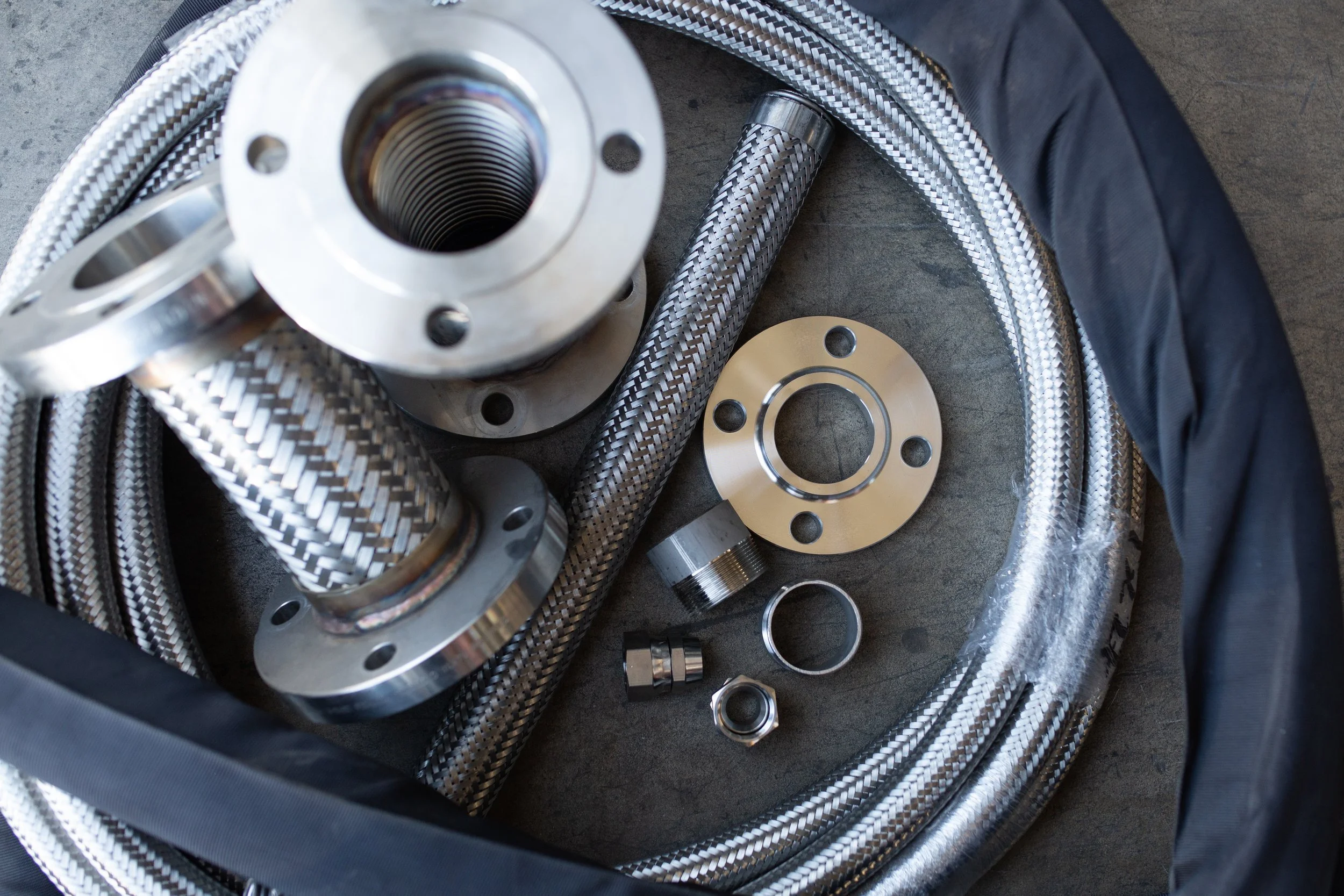 Various metal braided hoses and cylindrical components laid out on a dark surface.