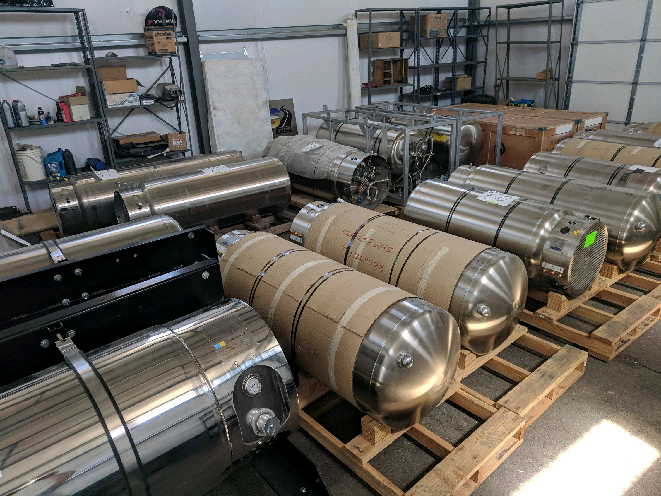 Assorted stainless steel tanks and equipment stored on wooden pallets in a workshop or warehouse.