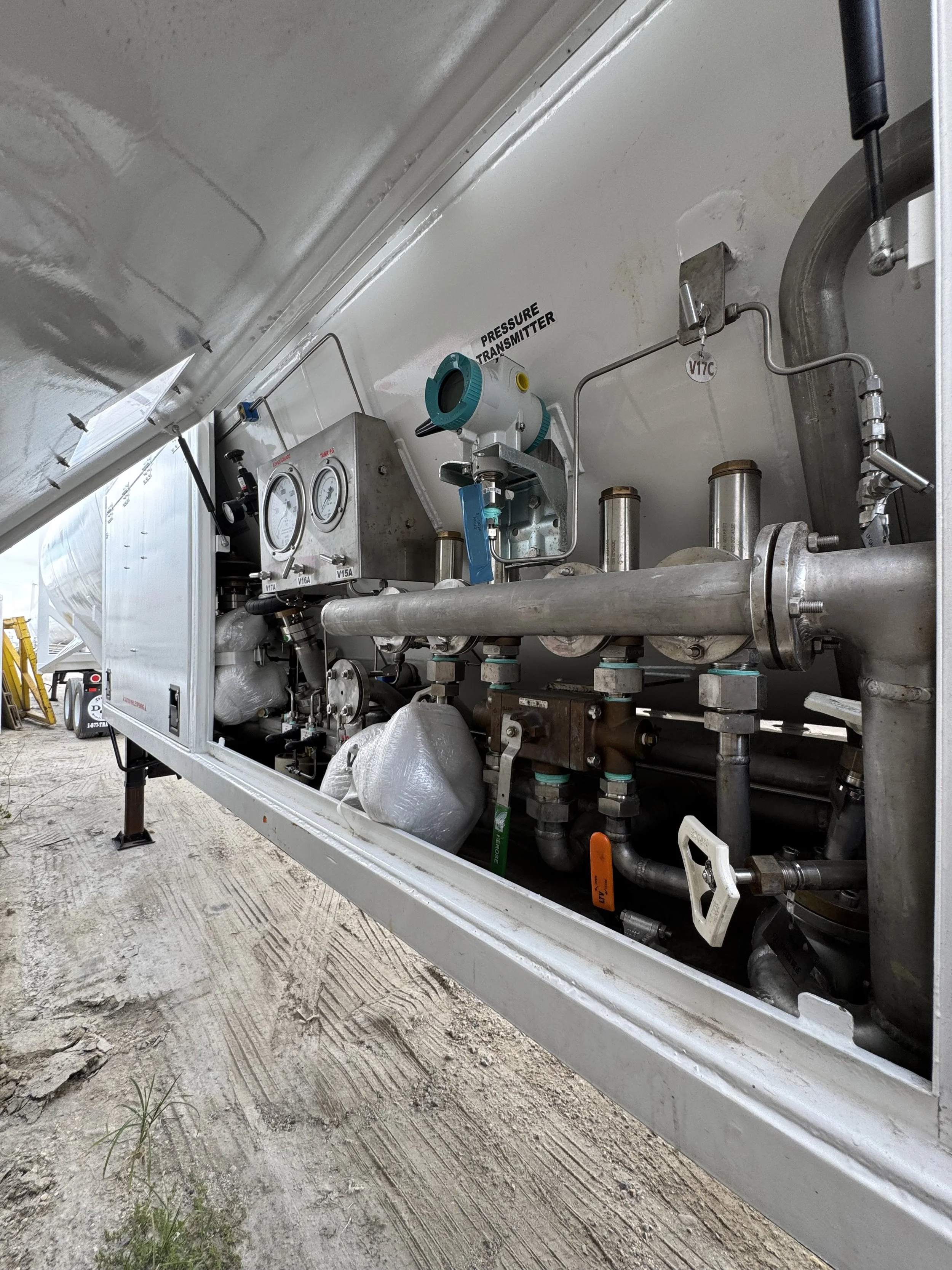 Open equipment compartment revealing pipes, gauges, and a pressure transmitter inside a mobile unit on a dirt surface.
