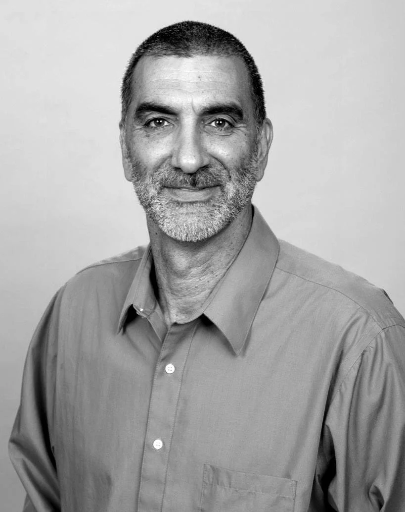 Black and white portrait of a middle-aged man with short dark hair and a beard, wearing a collared shirt, smiling at the camera.