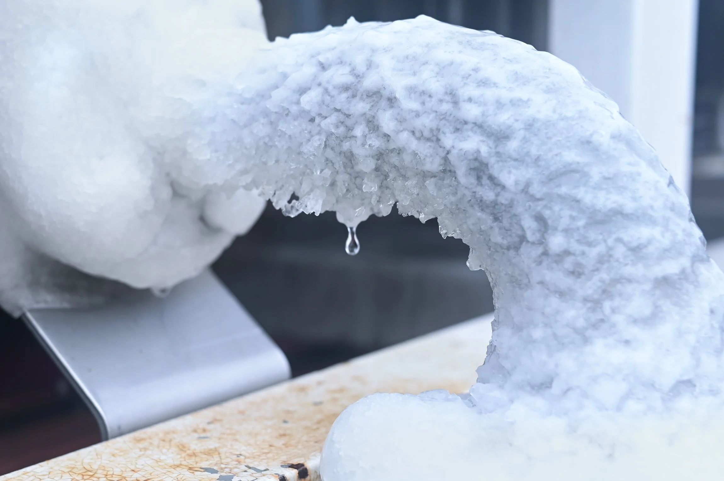 Close-up of a snow or ice sculpture with a water droplet freezing at the tip, showing detailed icy texture.