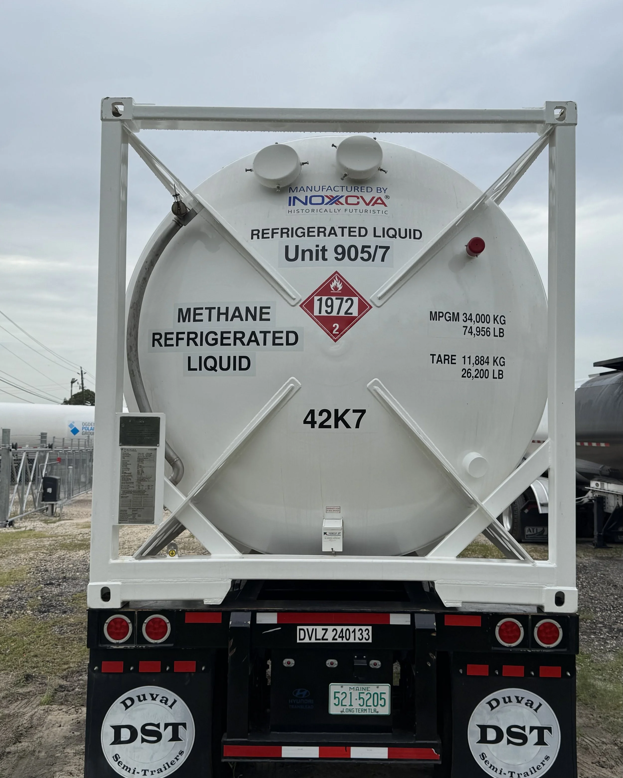 Rear view of a white tanker truck carrying refrigerated liquid methane, with safety and informational labels, including manufacturer, date, and weight ratings, parked outdoors.