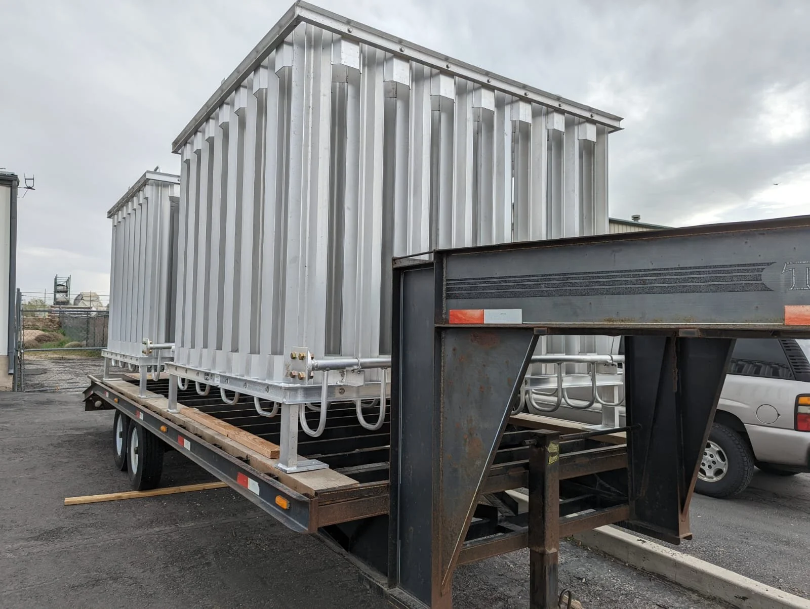 Two large metallic structures on a flatbed trailer, with a gray overcast sky in the background.