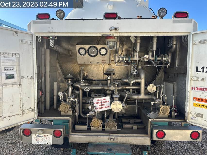 Open side of a mobile chemical or industrial processing unit with various metal pipes, gauges, and valves, including a sign indicating the trailer is pressurized with nitrogen.