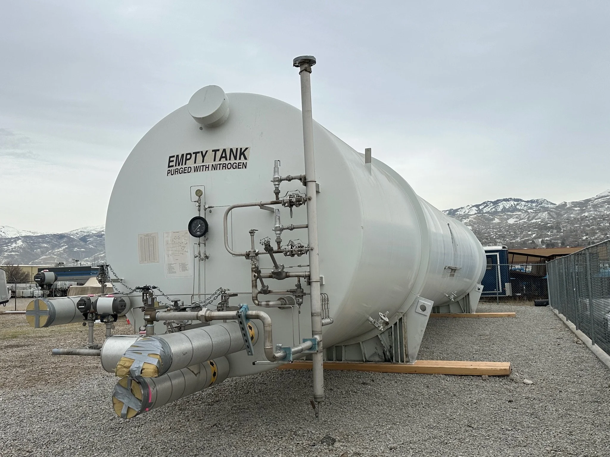 Large white tank labeled 'Empty Tank Purged with Nitrogen' outdoors, with pipes, gauges, and valves, mountains in the background.