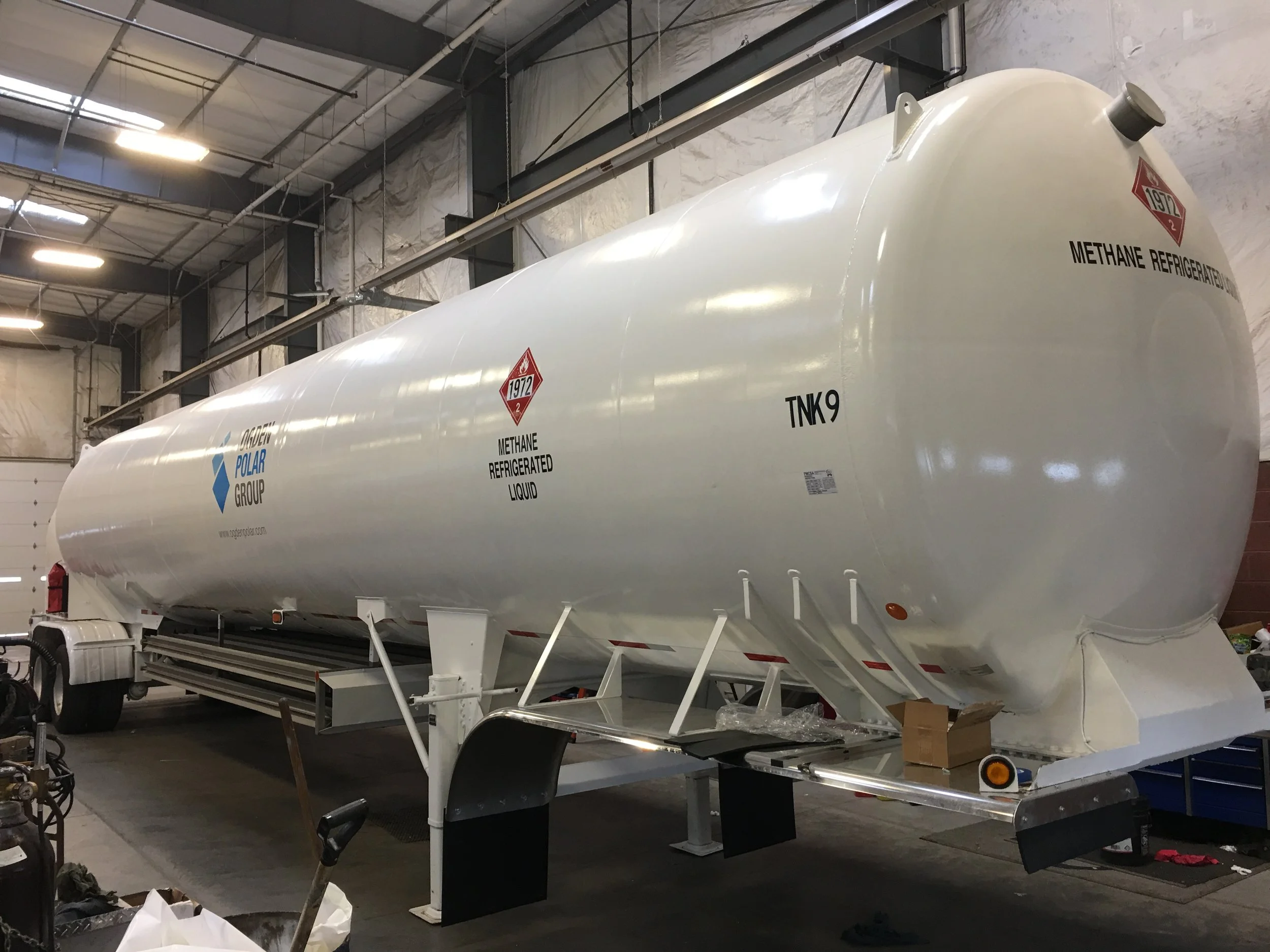 A large white methane refrigerated liquid tank inside a warehouse with high ceilings and bright lights, mounted on a trailer for transportation.