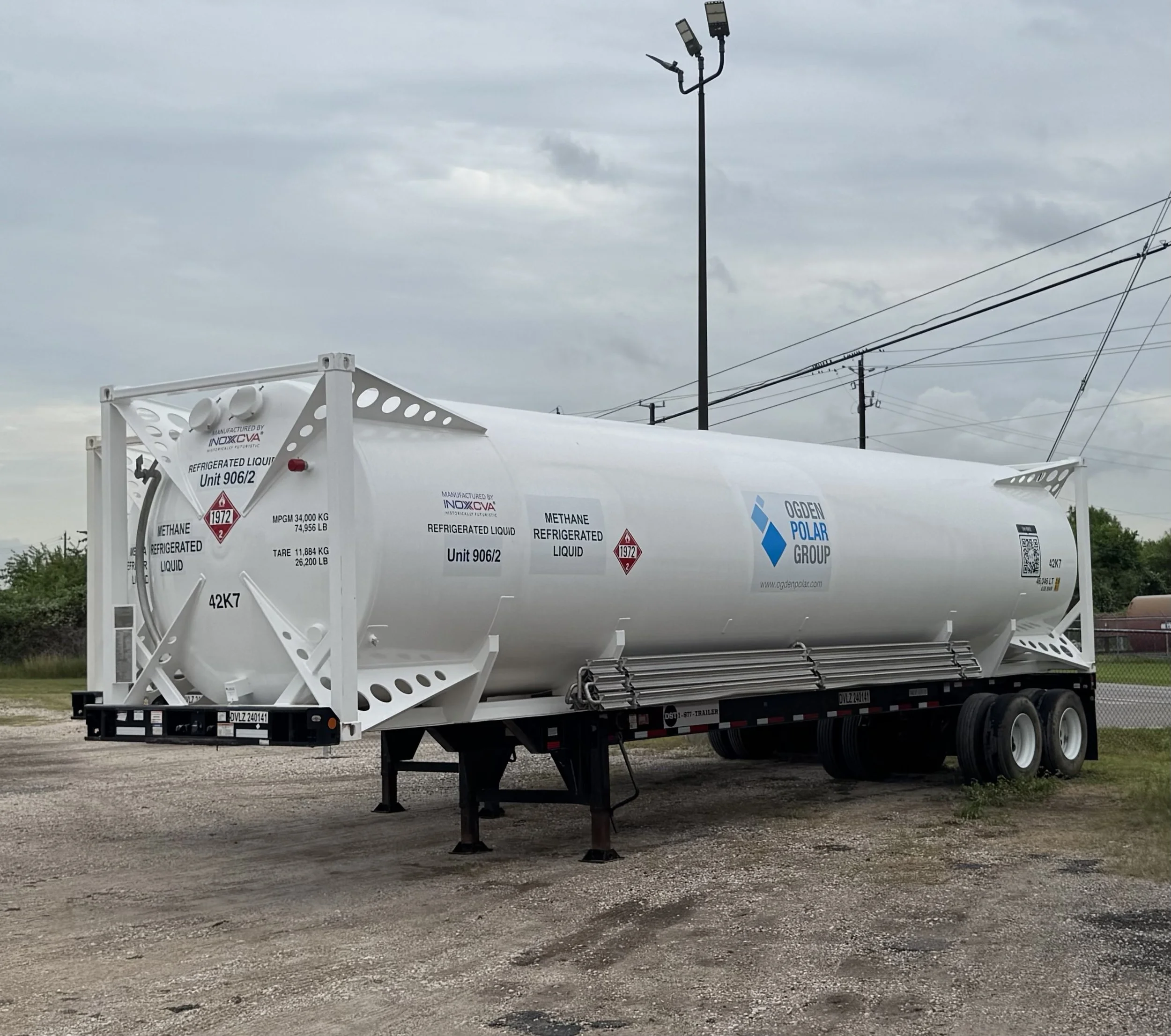 A large white tanker trailer used for transporting refrigerated liquid methane, with logos and safety markings, parked on gravel under cloudy skies.