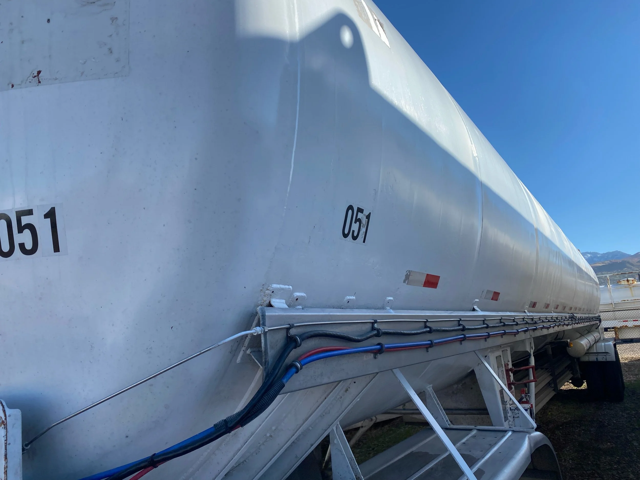 A large white tanker trailer with the identification number '051' on its side, parked outdoors with mountains visible in the background and clear blue skies overhead.
