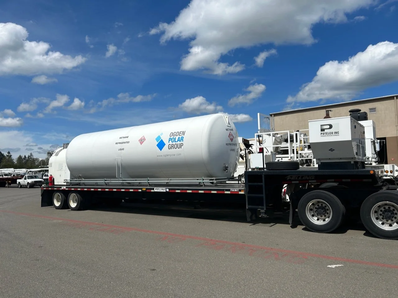 A large tanker truck on a parking lot carrying liquefied natural gas, with a blue sky and clouds overhead.