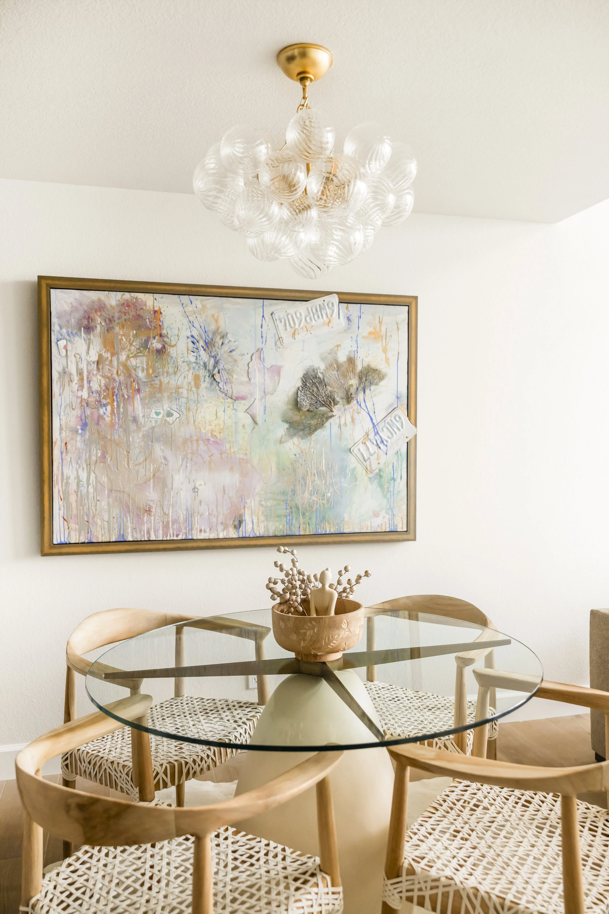 Interior photo of condo with glass dining table, rattan chairs, bubble chandelier and abstract art
