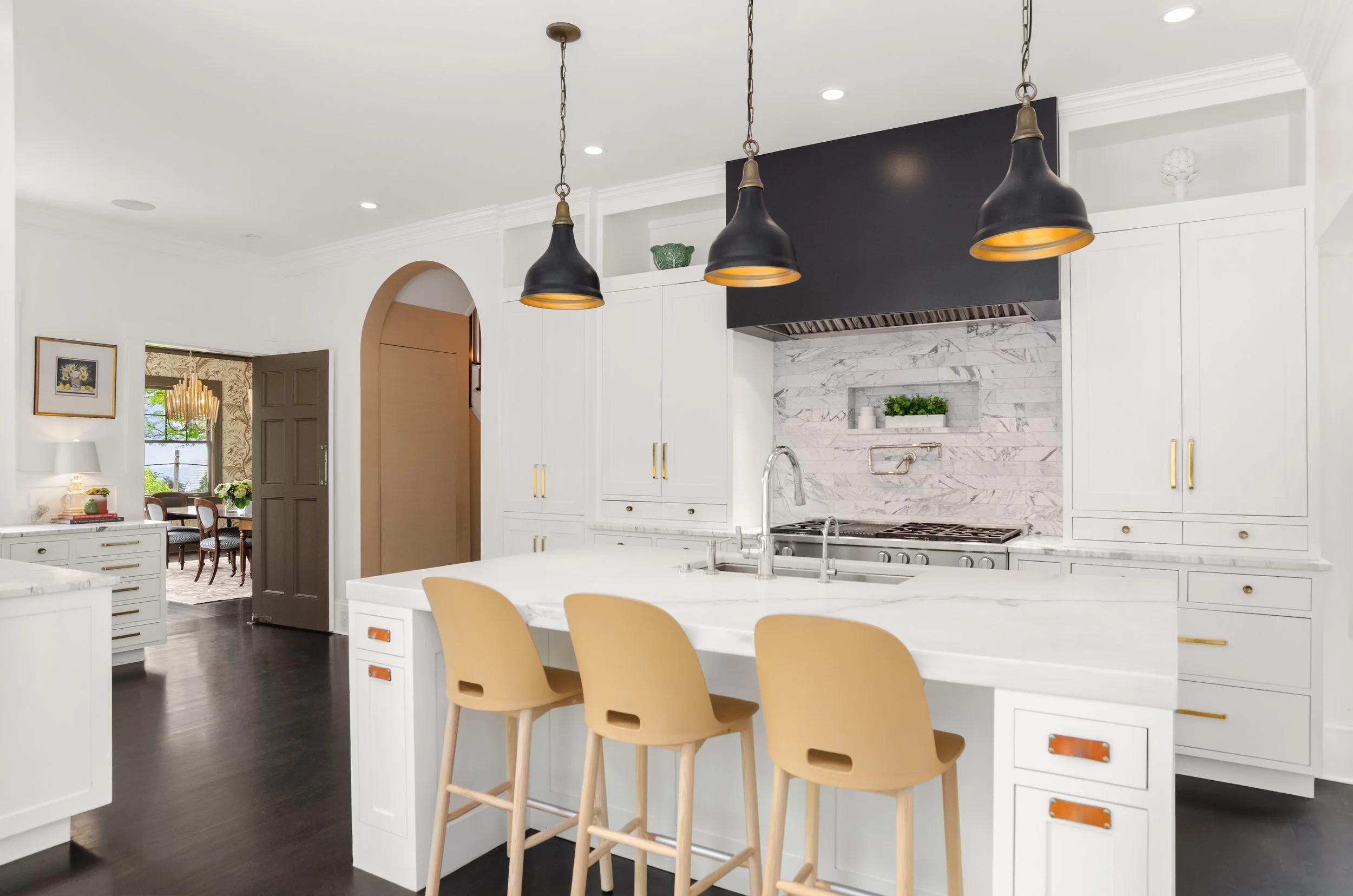 Modern kitchen with white cabinets, marble backsplash, black pendant lights, and beige bar stools at a white marble island.