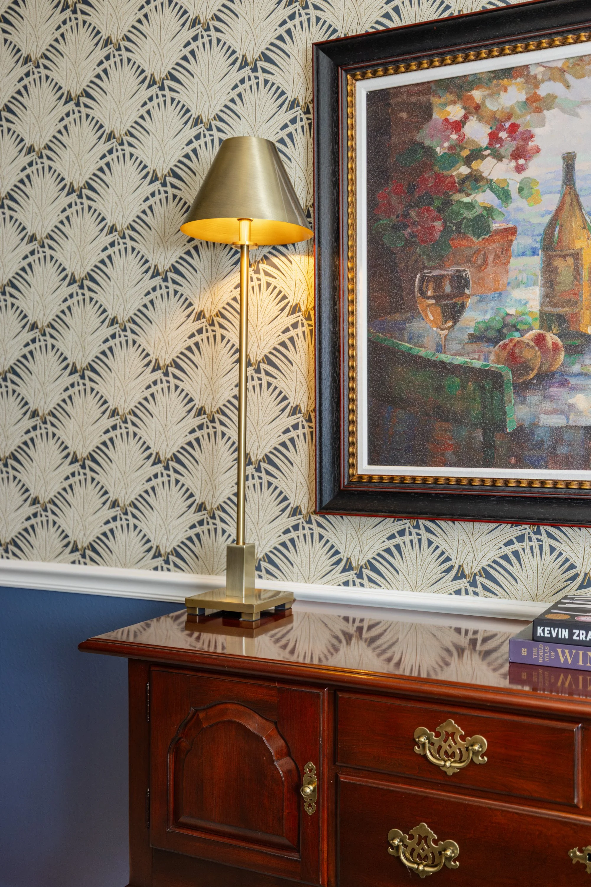 traditional sideboard, wallpaper and blue paint and brass lamp with painting of vineyard and wine