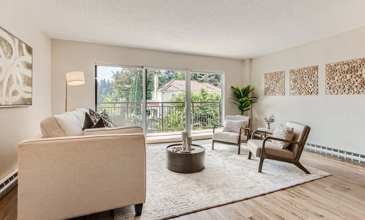 Living room with cream sofa, two armchairs, a rug, glass sliding door leading to balcony, and framed artwork on the walls.