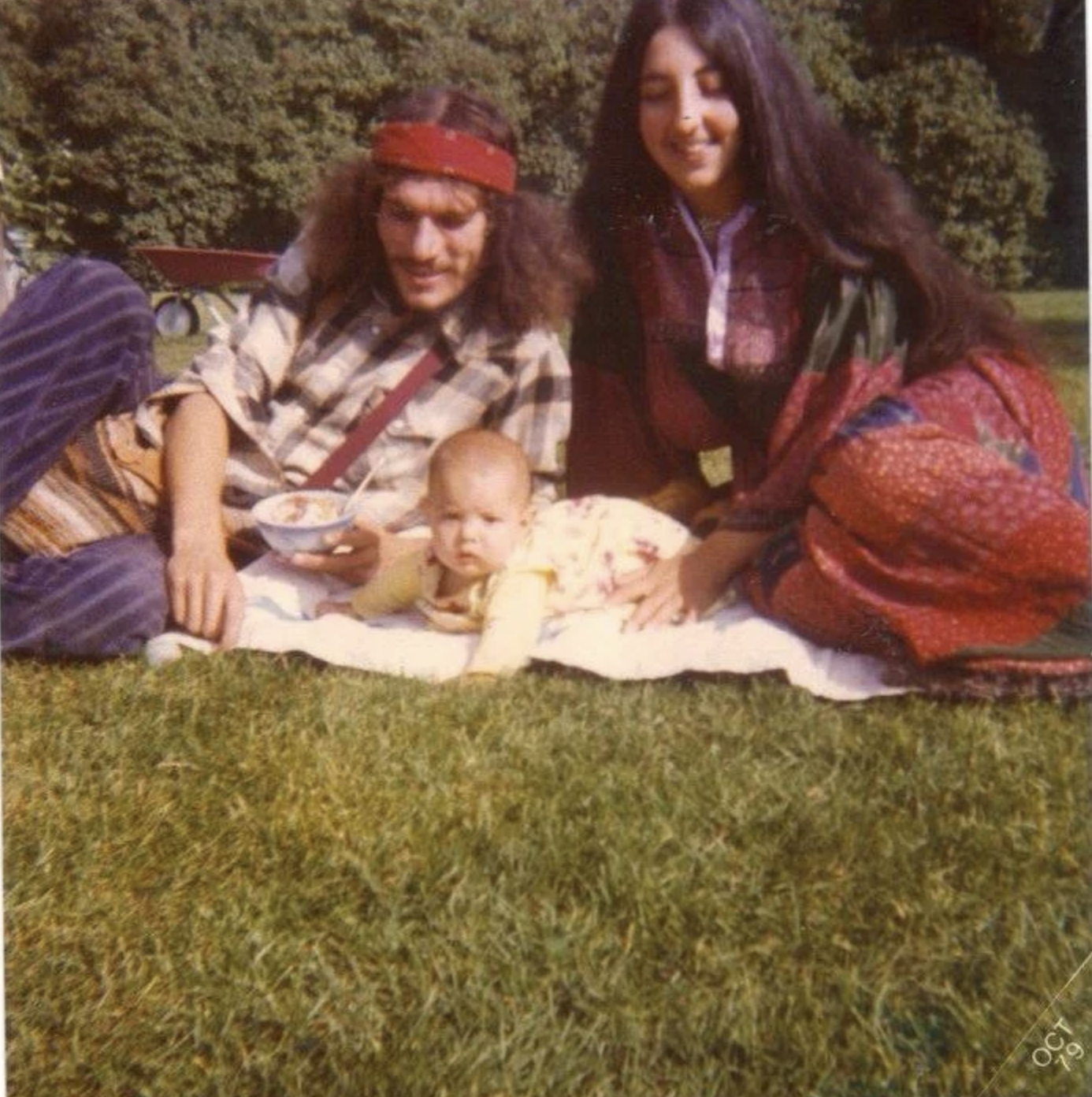 Picture of 1970's hippie parents with a baby on a blanket in the grass