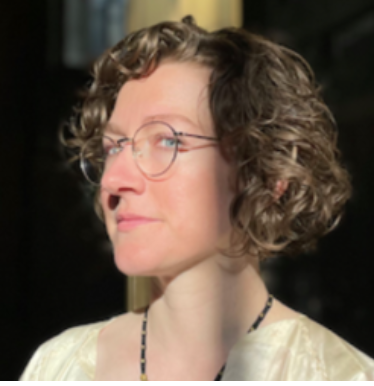 young woman with a bob with glasses and wavy hair as the sun hits her face smiling