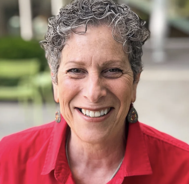 woman with short wavy black and gray hair wearing a red shirt smiling