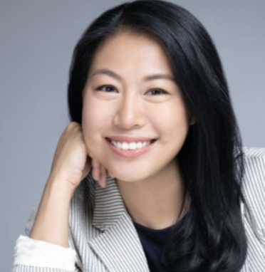 asian woman with black hair in a suit with her hand resting on her cheek smiling
