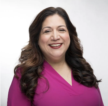 Latine woman with long brown wavy hair with a fushia blouse smiling