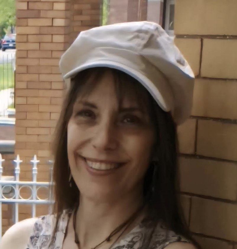 woman with white hat and brown hair posing in front of a brick wall