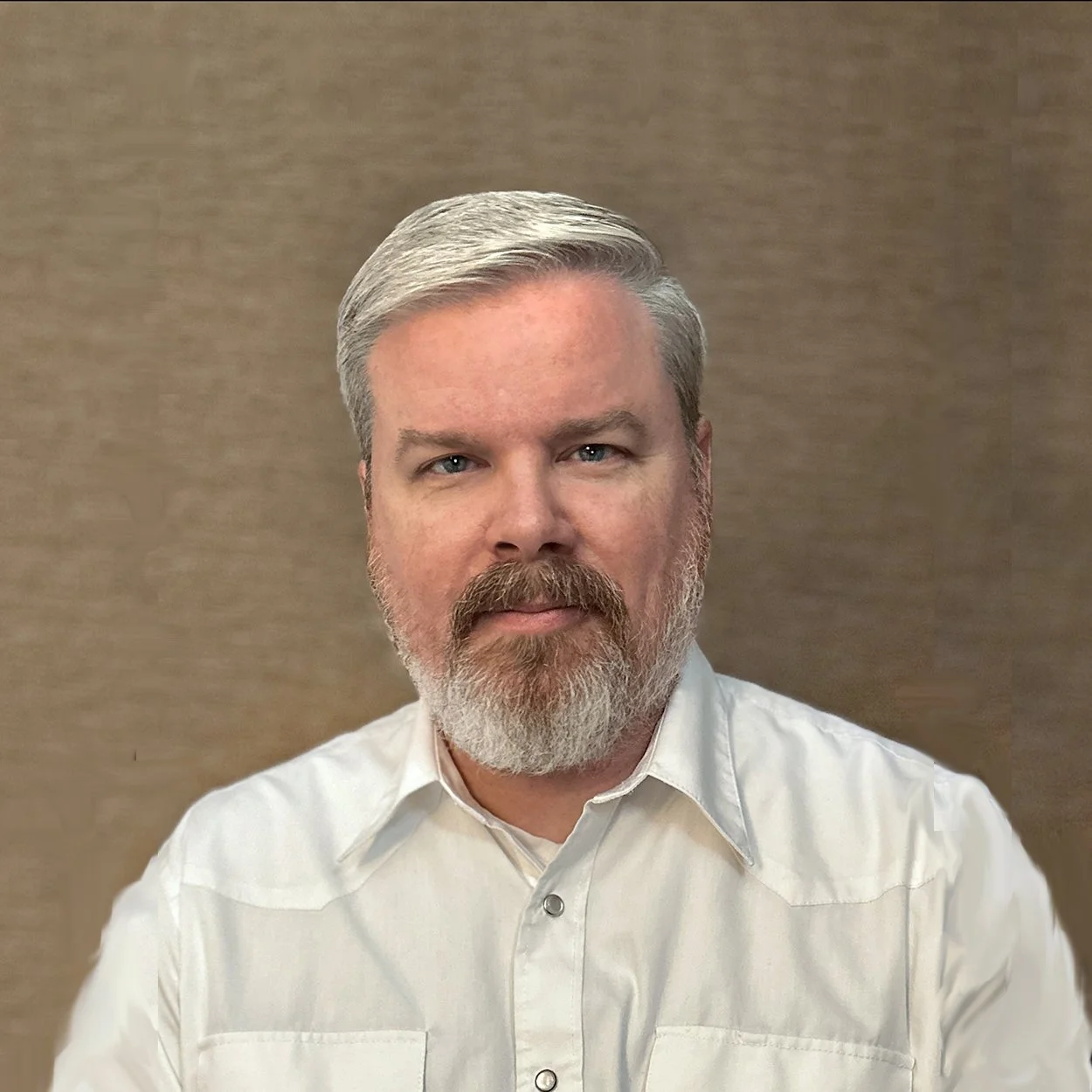 A man with gray hair and a beard wearing a white shirt against a beige background.