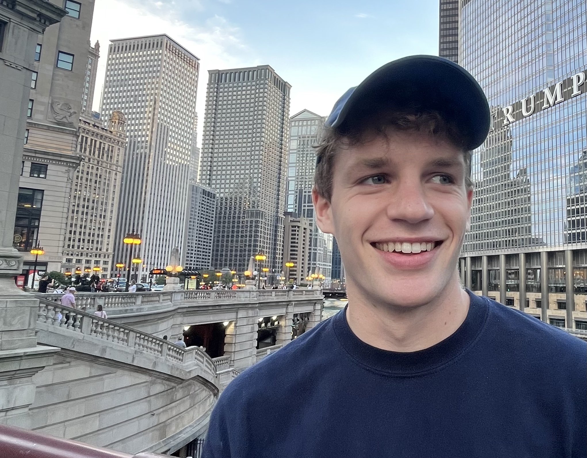 young man in a baseball cap smiling in front of city buildings