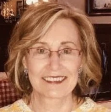 older woman with blonde hair and glasses smiling for the camera