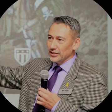 Man in a gray suit with purple tie holding a microphone