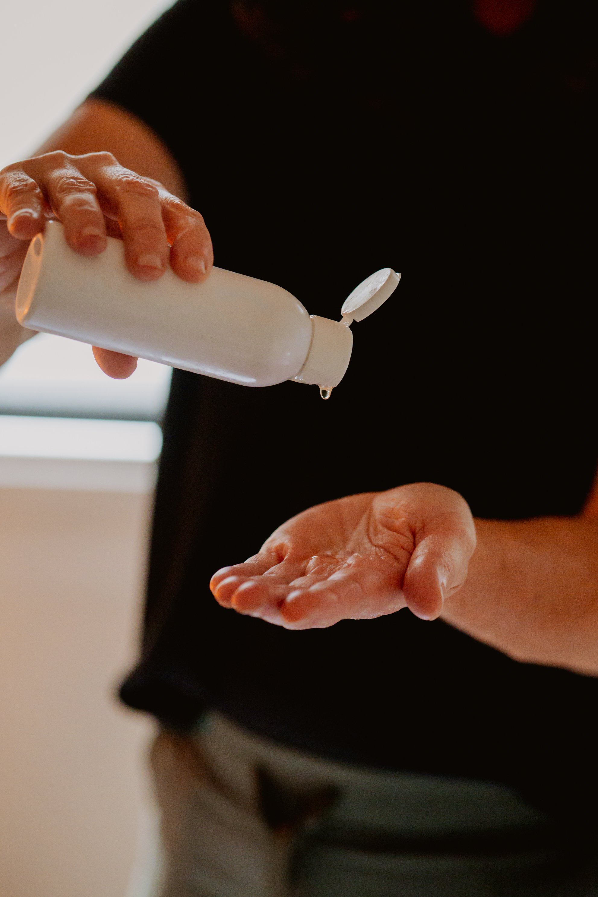 A person dispensing hand sanitizer into their open palm from a white bottle.